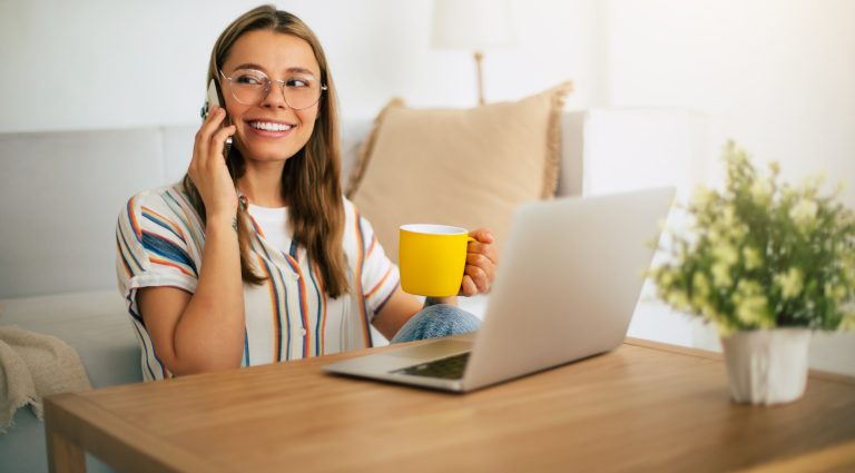 Cute blonde smiling woman with glasses sits at a wooden desk, ta